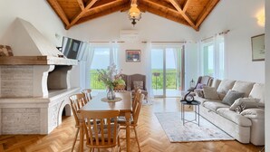 Amplia sala de estar con techo de madera alto, chimenea, mesa de comedor con sillas y sofá.