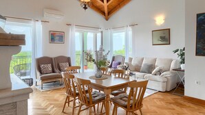 Un salón comedor amplio con techo de madera, una mesa de comedor con sillas, un conjunto de sofás y un balcón con vistas.