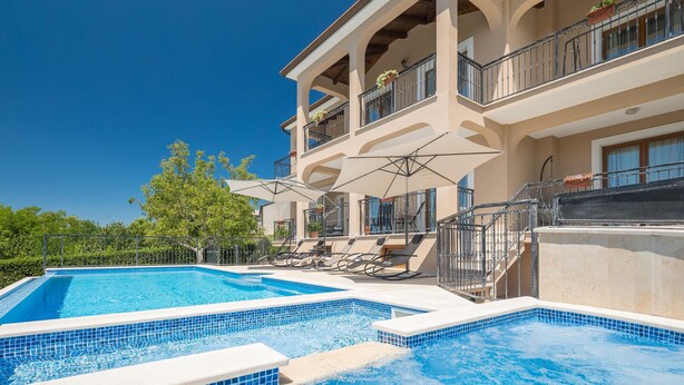 Un hotel con piscina, mobiliario exterior y un balcón con macetas.