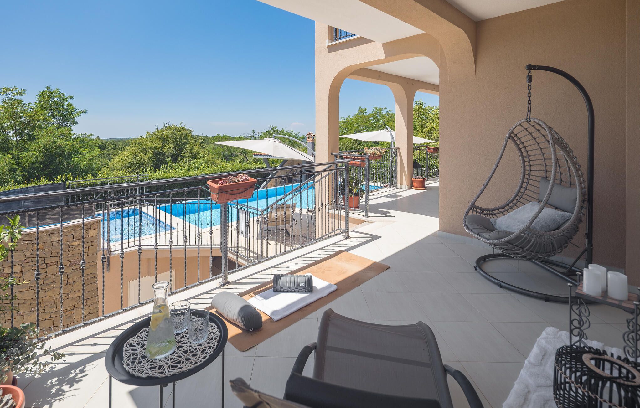 Un balcón con piscina, una silla colgante y una mesa con una botella y vasos.