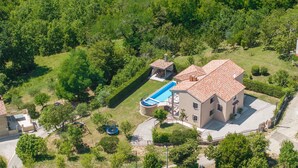 Una casa de dos pisos con piscina, rodeada de abundante vegetación.