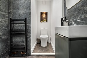 A modern bathroom with a black towel rack, a toilet, and a bathtub. - Immaculate 6-bed House in Newcastle (Wallsend)