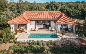 Ein zweistöckiges Haus mit Ziegeldach, Schwimmbad und einer Terrasse mit Gartenmöbeln.
