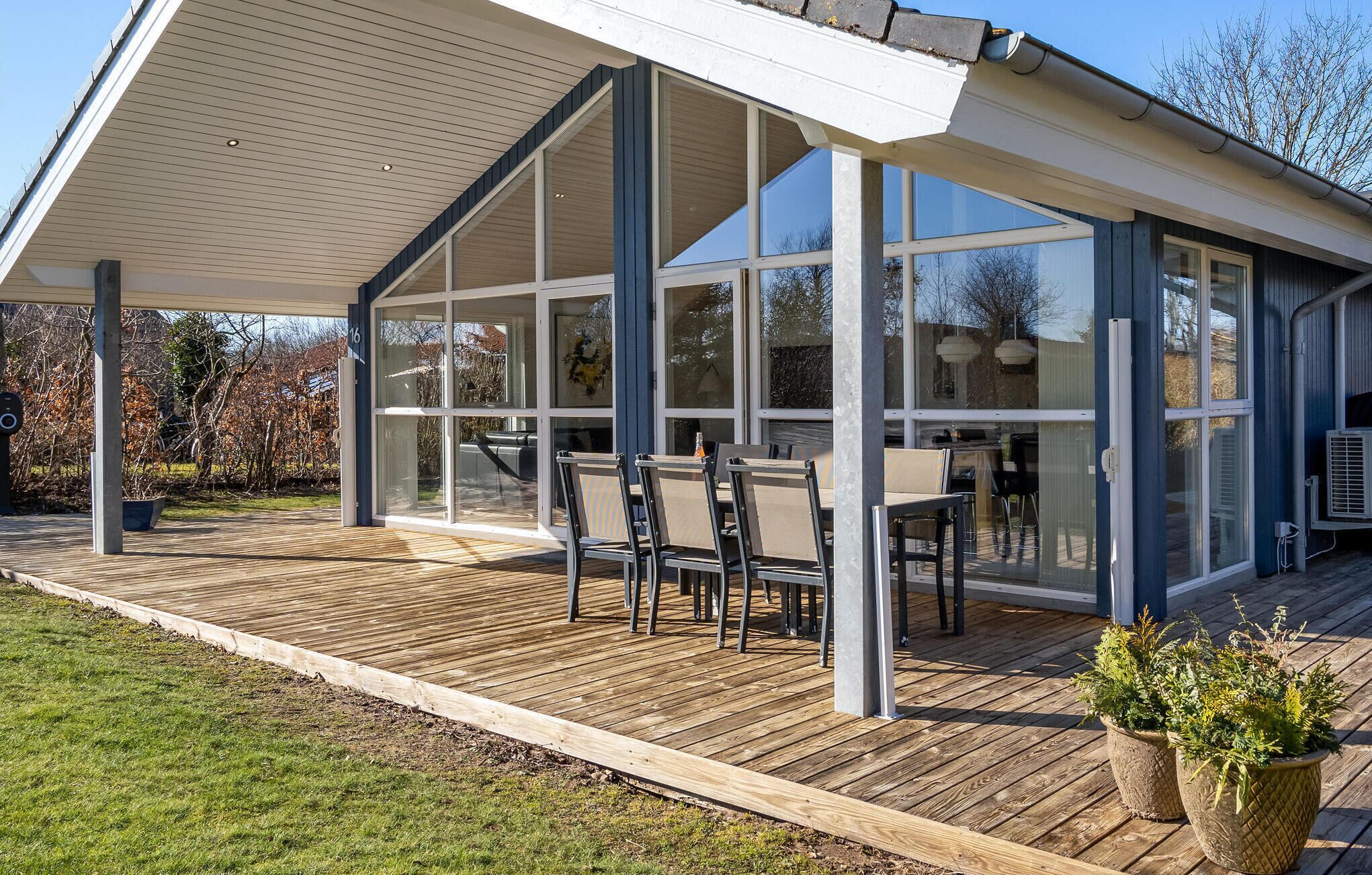 A covered outdoor area with a wooden deck, glass walls, and a table with chairs.