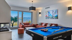 A modern living room with a pool table, a sofa, and a large window offering a scenic view. - Villa Sauvignon (Motovun)