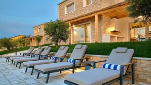 A row of sun loungers with cushions, a stone building with a stone facade, and a well-maintained hedge in front. - Villa Sauvignon (Motovun)