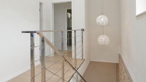 A modern interior with a glass railing staircase, a hallway leading to a room, and two spherical pendant lights. - Villa Sauvignon (Motovun)
