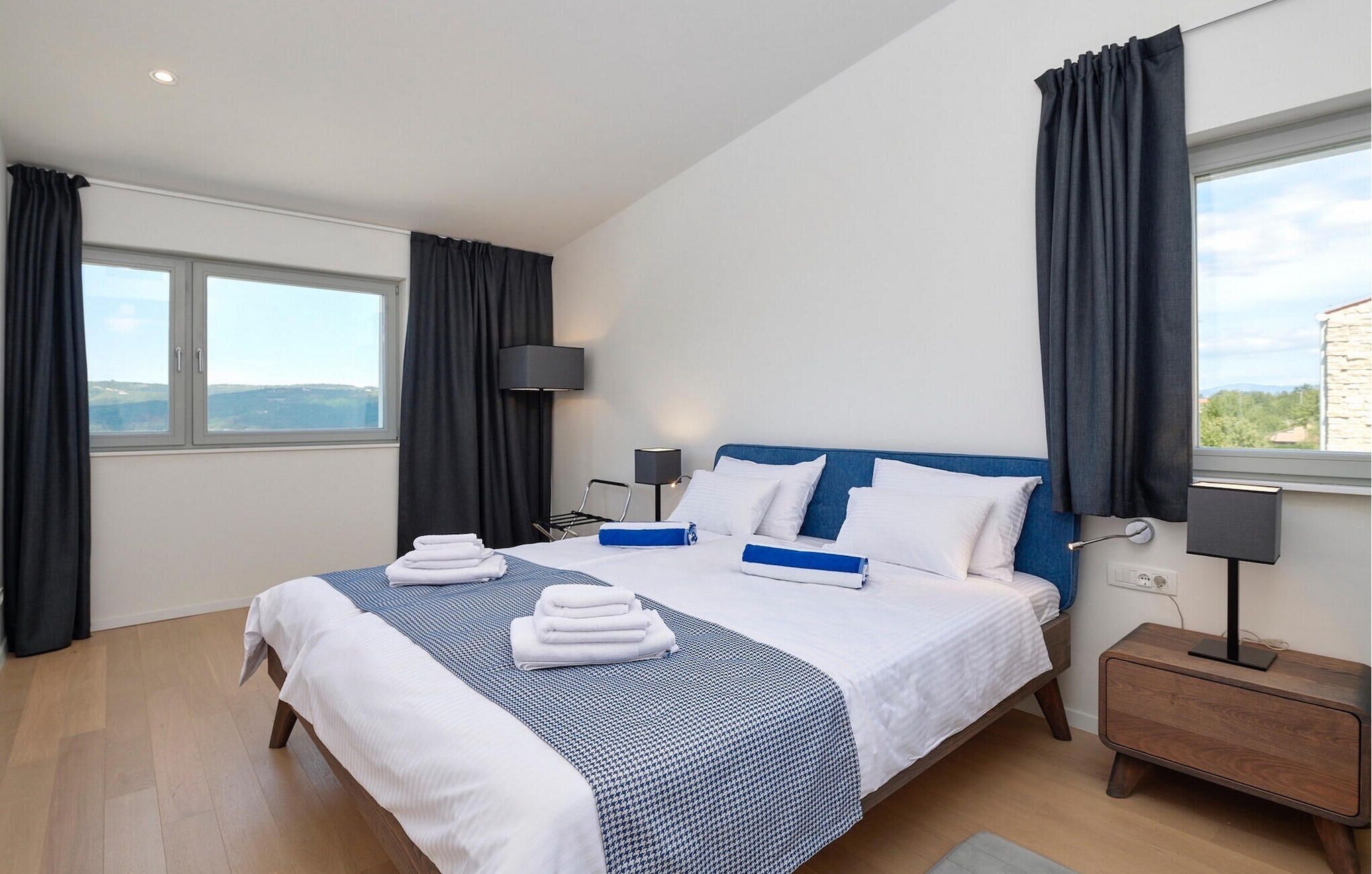 A modern hotel room with a large bed, two bedside tables, a nightstand, and a view of the landscape.