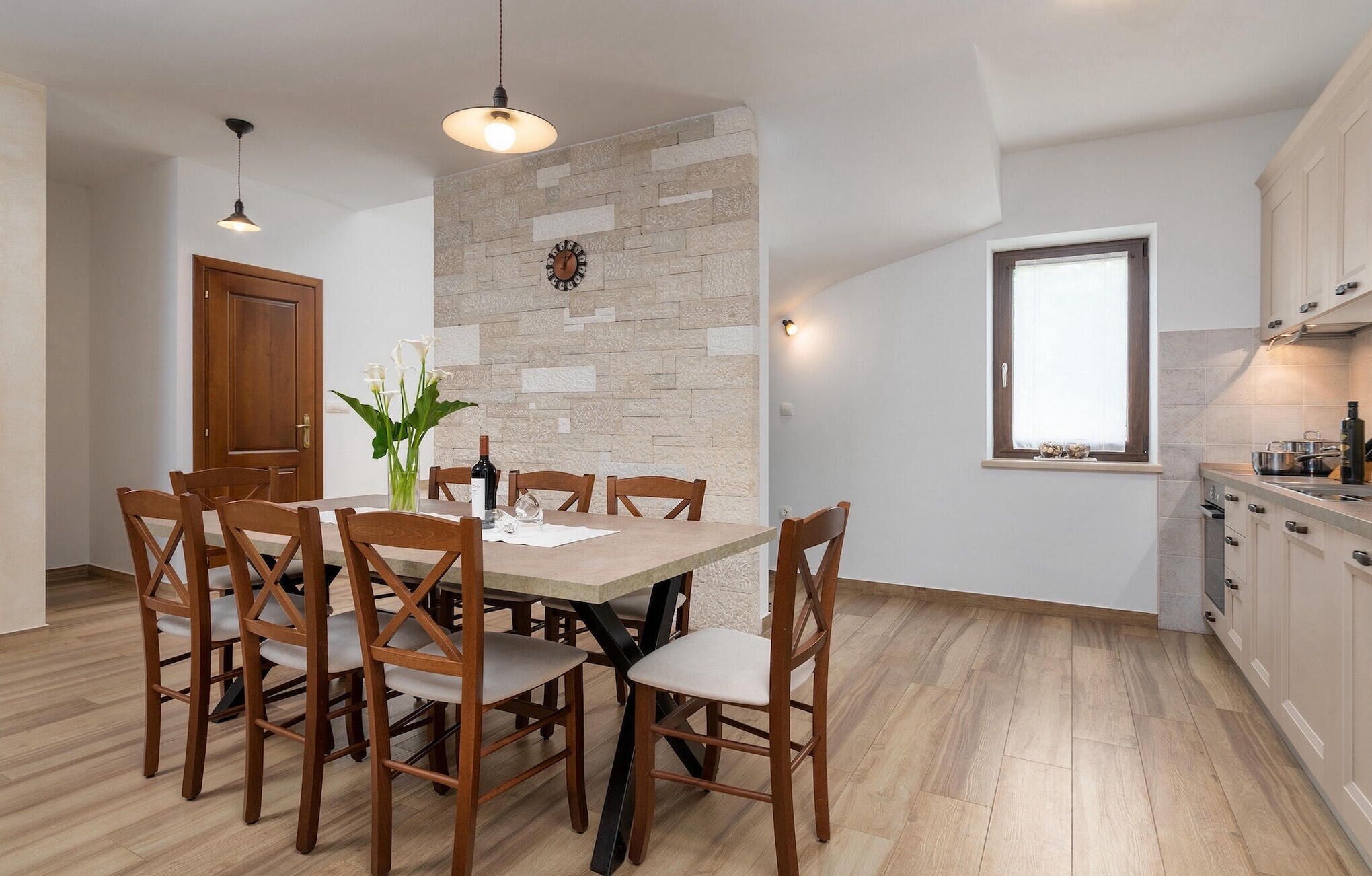 A dining area with a wooden table and chairs, a vase with flowers, and a stone wall.