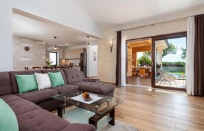 Ein modernes Wohnzimmer mit einem Ecksofa, einem Glastisch und Blick auf eine Terrasse mit Gartenmöbeln.