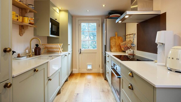 A narrow kitchen with white cabinets, a built-in oven, and a window. - Sunshine Joy, by Veeve (London)