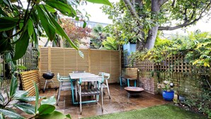 A patio with a wooden table and chairs, a wheelbarrow, and a potted plant. - Sunshine Joy, by Veeve (London)