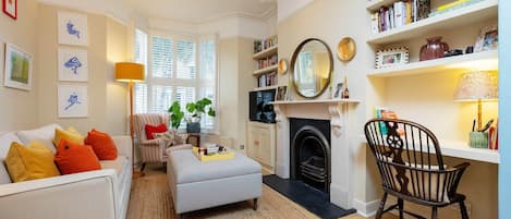 A living room with a sofa, ottoman, and a fireplace. There are bookshelves and a chair.