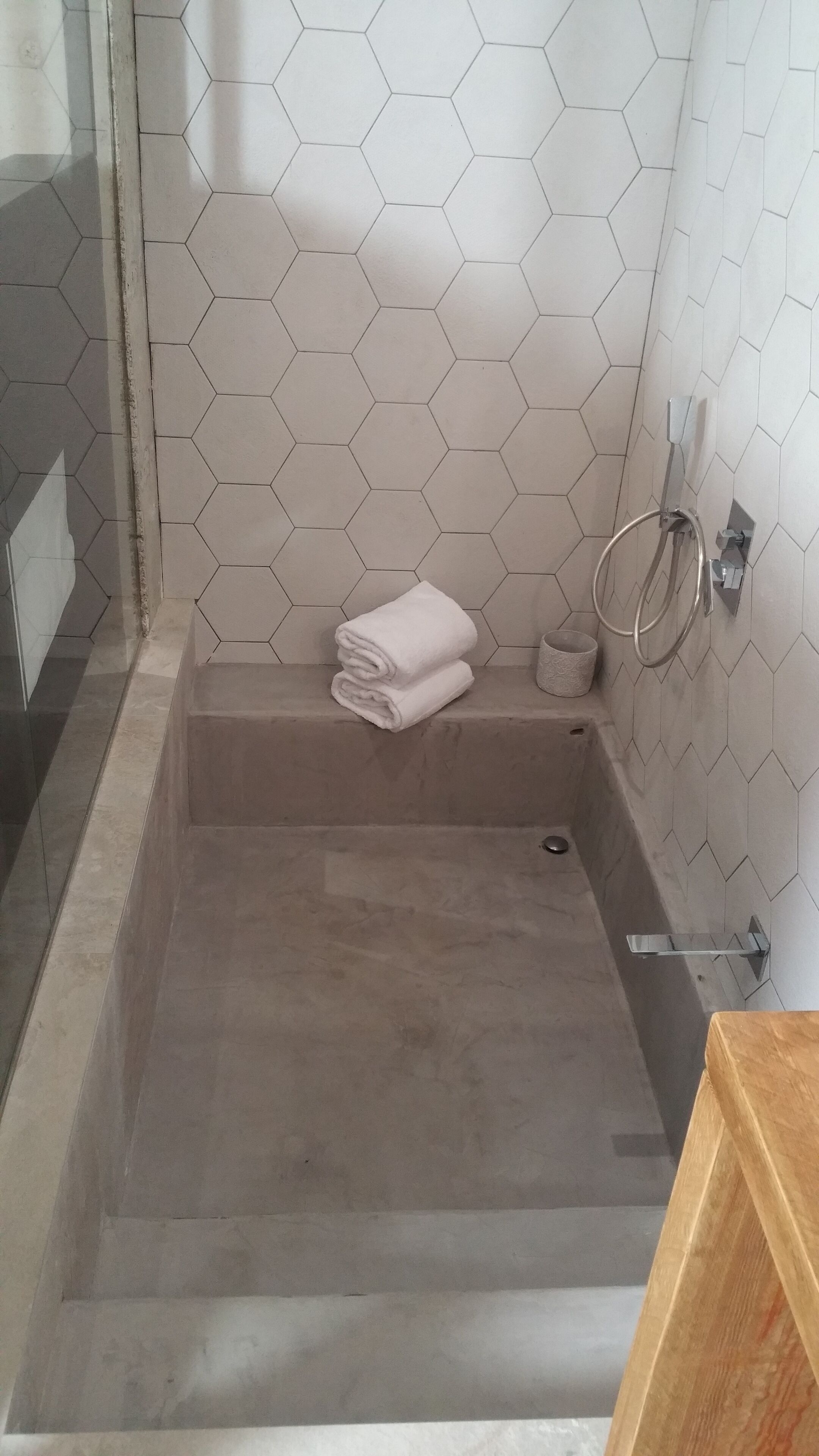 Un baño con pared de azulejos hexagonales, cabina de ducha de vidrio y tocador de madera.