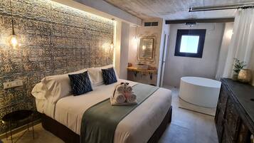 Un dormitorio moderno con pared estampada, una cama con almohadas, una mesita de noche, un espejo, una ventana y un baño con lavabo e inodoro.