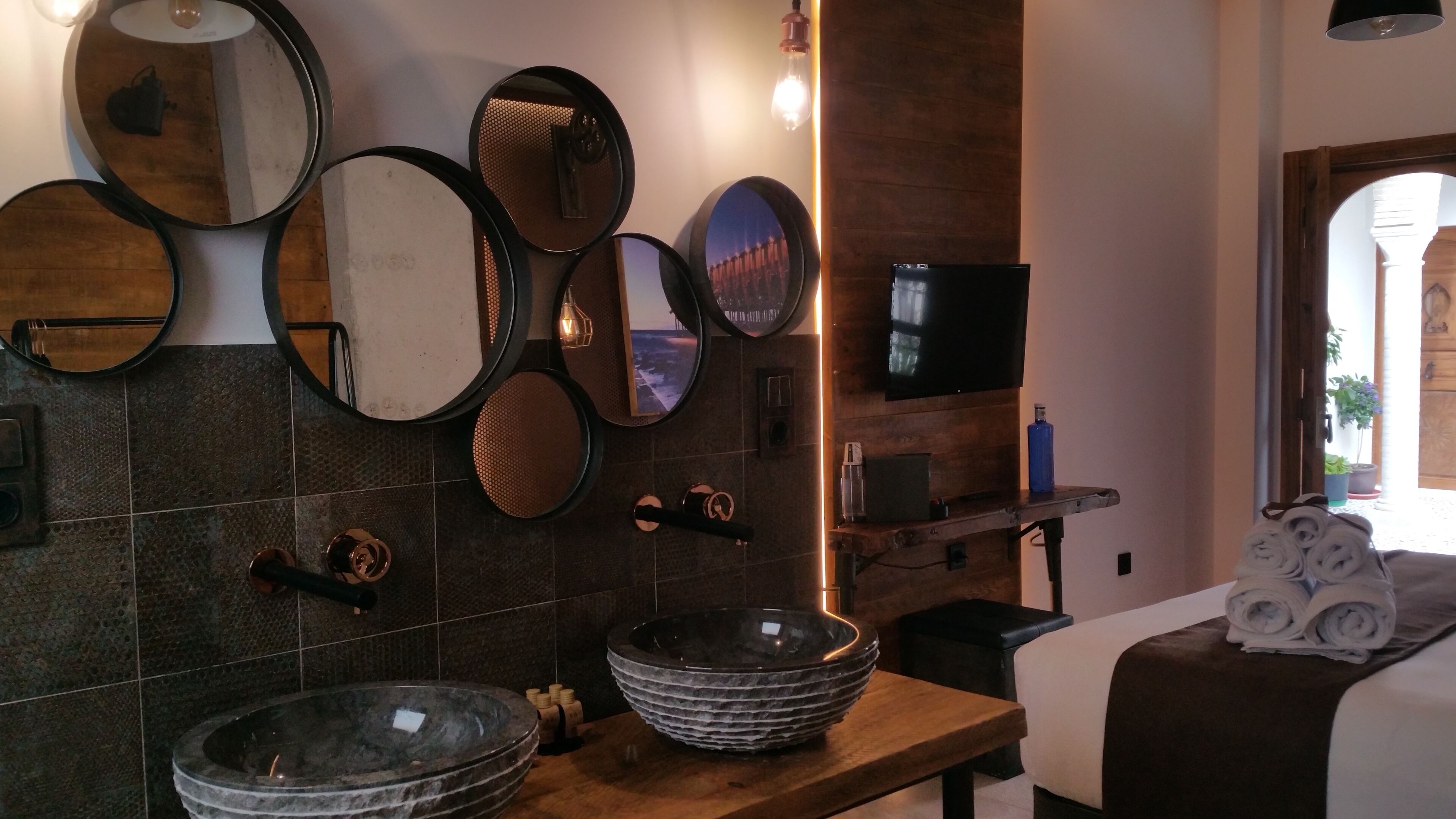 A modern bathroom with a stone sink, multiple mirrors, a television, and a wooden vanity.