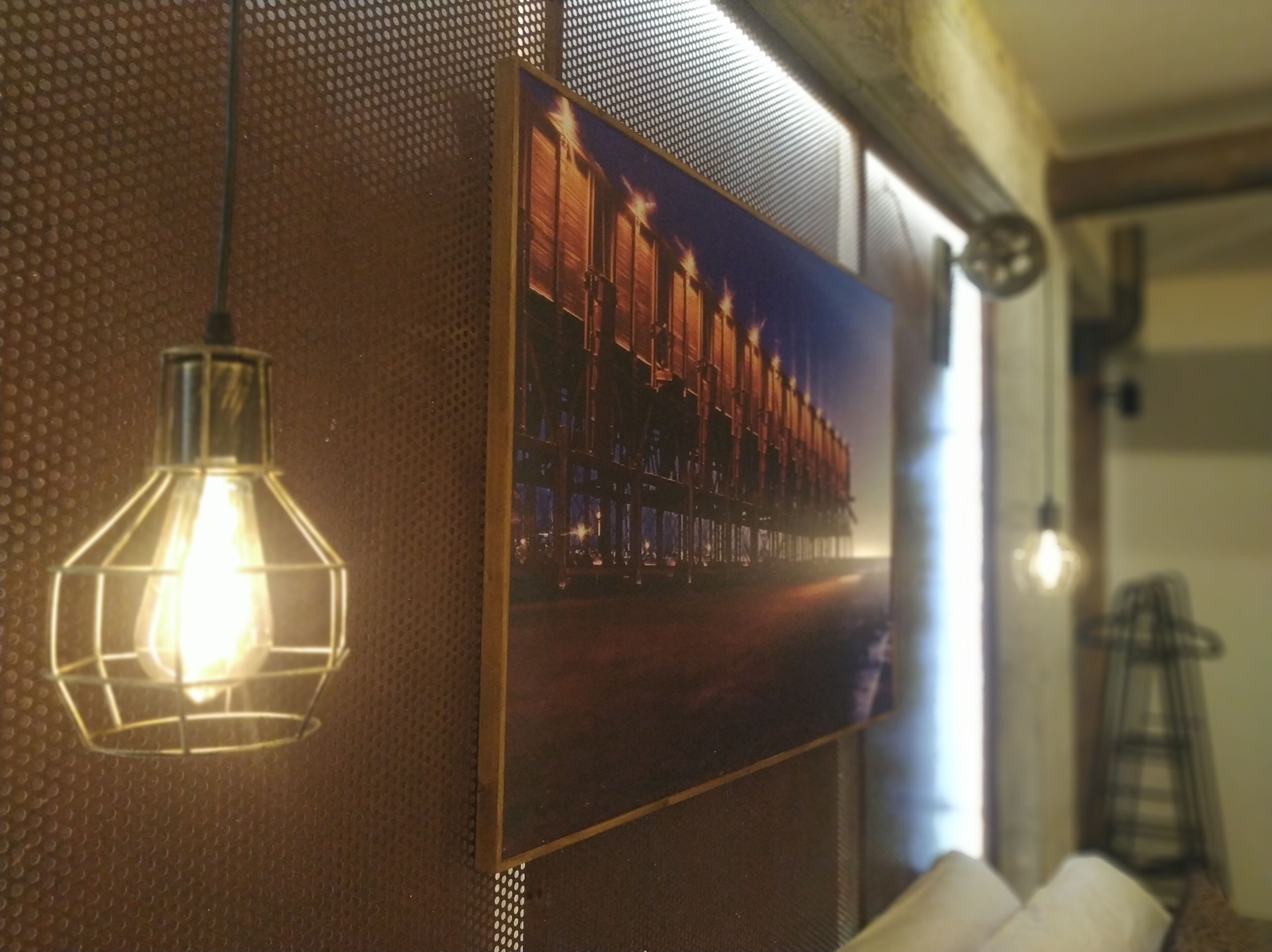 A framed picture of a train on a wall, a hanging light fixture, and a metal ladder.