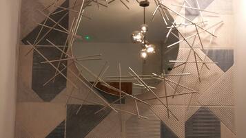 A modern bathroom with a geometric patterned wall, a round mirror, and a contemporary light fixture.