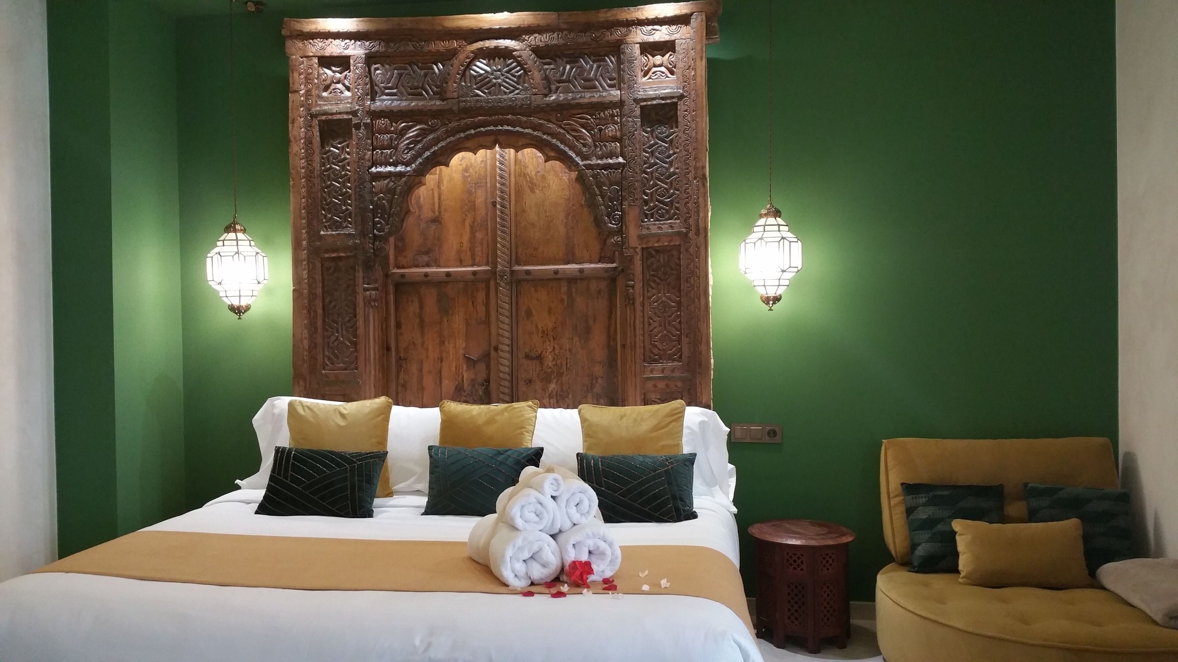 Une chambre d’hôtel avec une grande tête de lit en bois, un lit avec une literie blanche et dorée, et deux lampes fixées au mur.