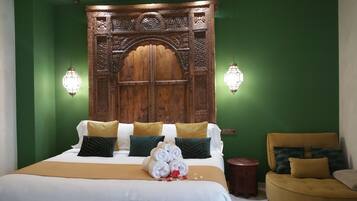 Une chambre d’hôtel avec une grande tête de lit en bois, un lit avec une literie blanche et dorée, et deux lampes fixées au mur.