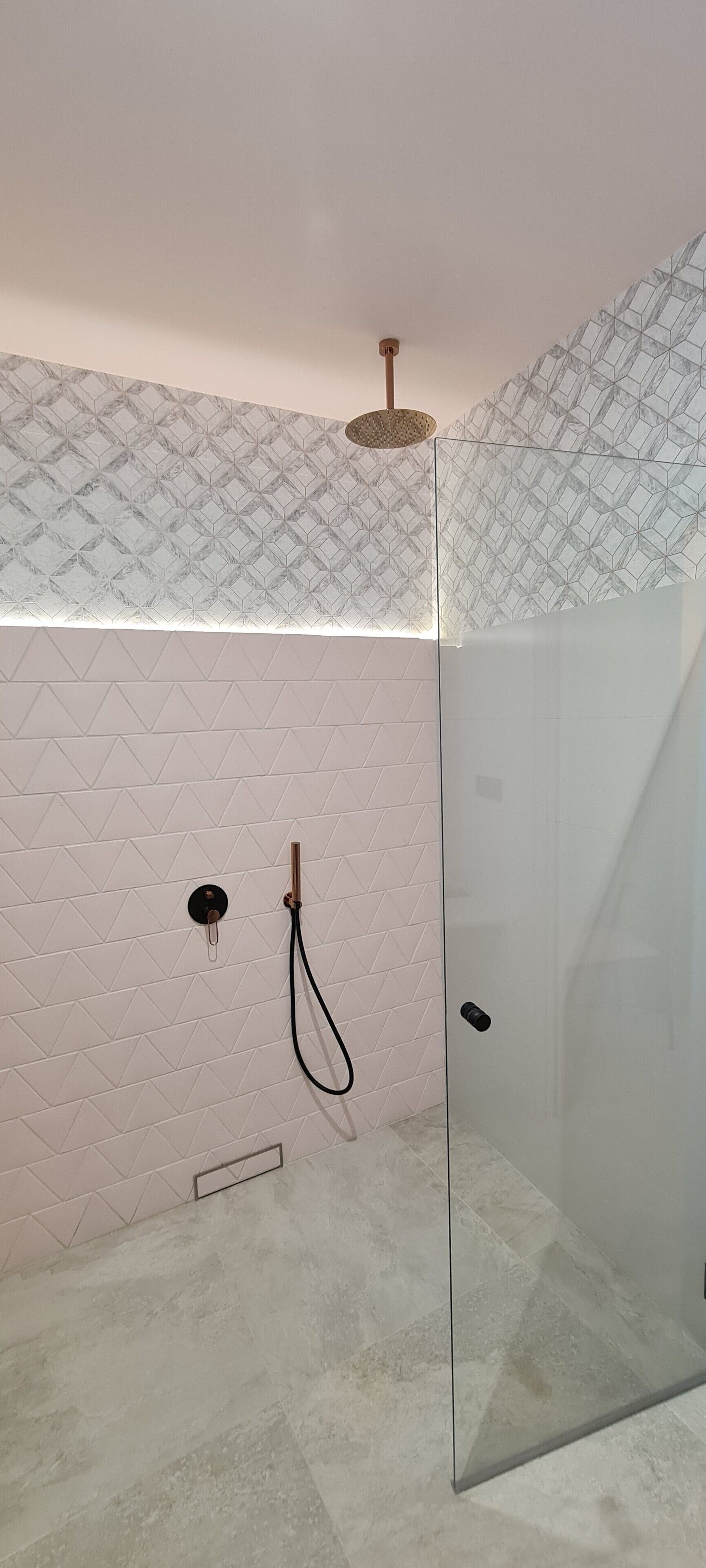 Una ducha moderna con puerta de vidrio, pared con patrón geométrico y diseño minimalista.