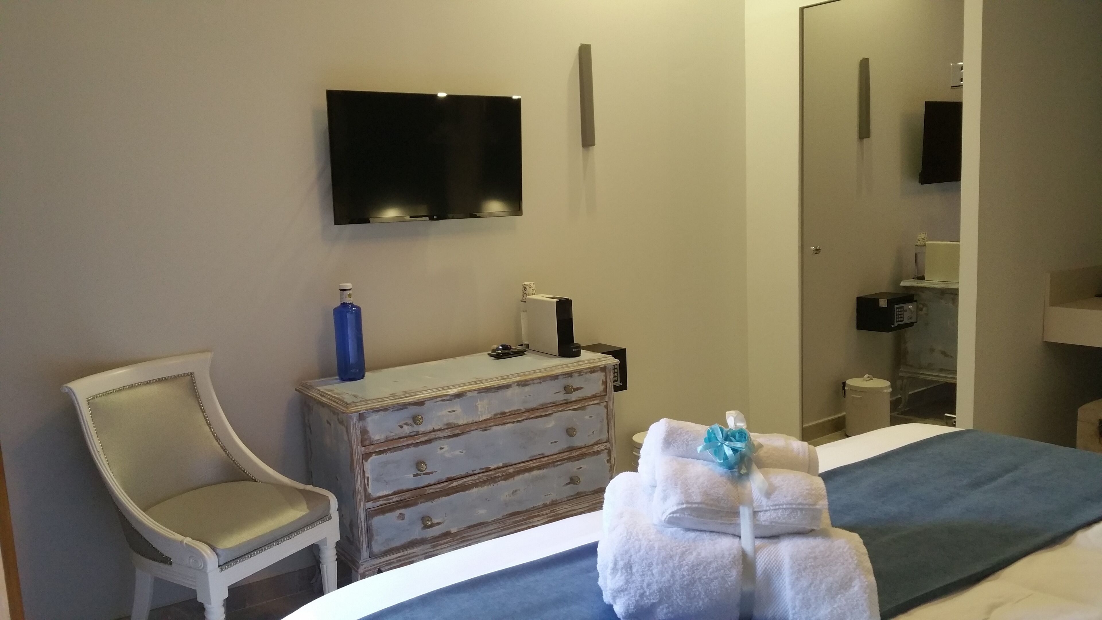 A hotel room with a bed, a chair, a dresser, a television, and a bathroom visible through an open door.