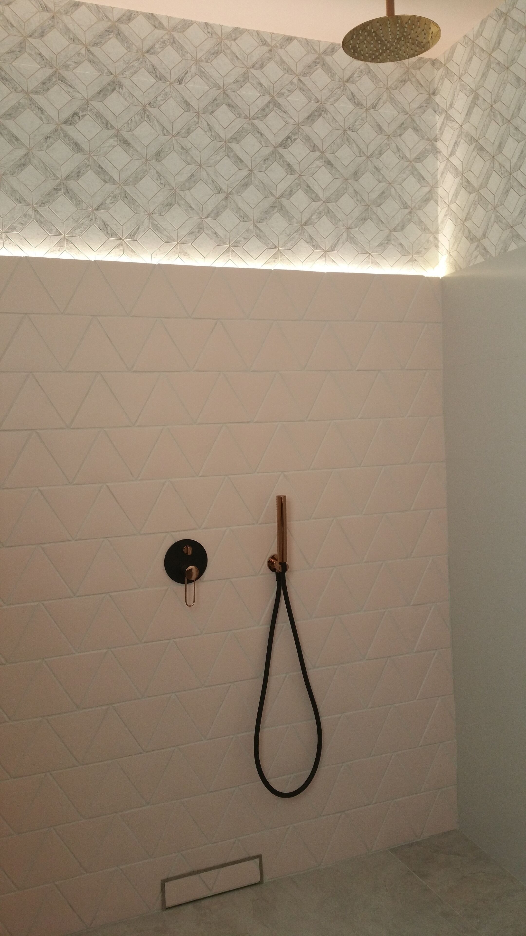 Une douche avec un carrelage mural aux motifs géométriques, une douchette à main et un robinet de réglage.
