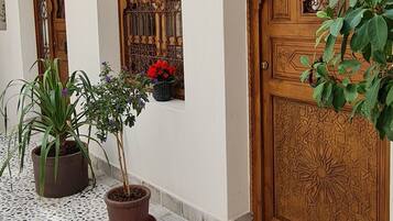 Un couloir doté d’un sol en terrazzo, de portes en bois ornées de sculptures complexes et de plantes en pot.