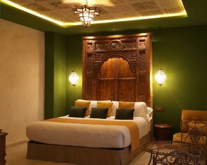 A bedroom with a large bed, green walls, and a wooden headboard with intricate carvings. - Murallas de Jayran Hotel Boutique (Almeria)