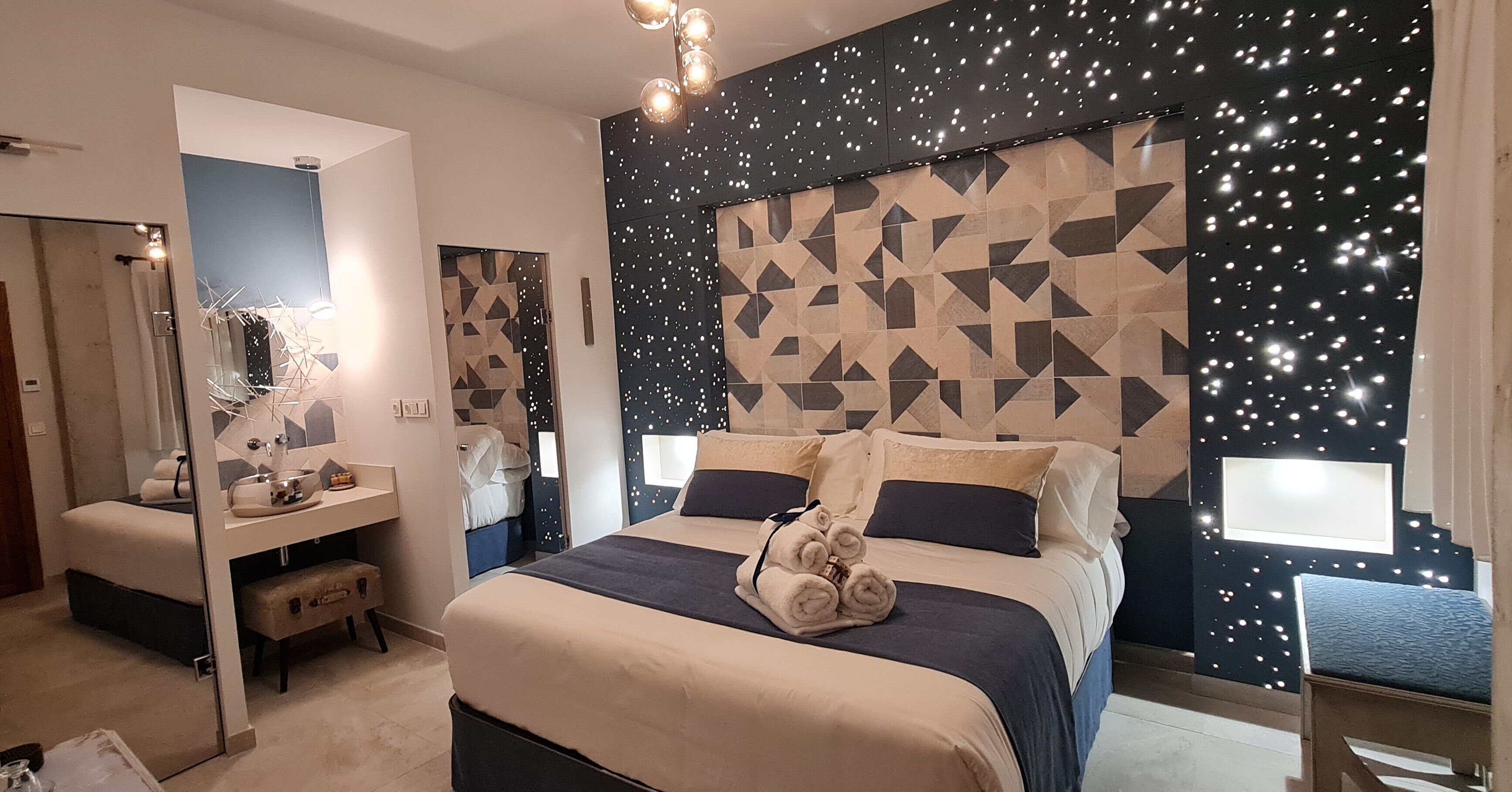 Een moderne hotelkamer met een groot bed, een kaptafel met spiegel en een hoofdbord met een geometrisch patroon.