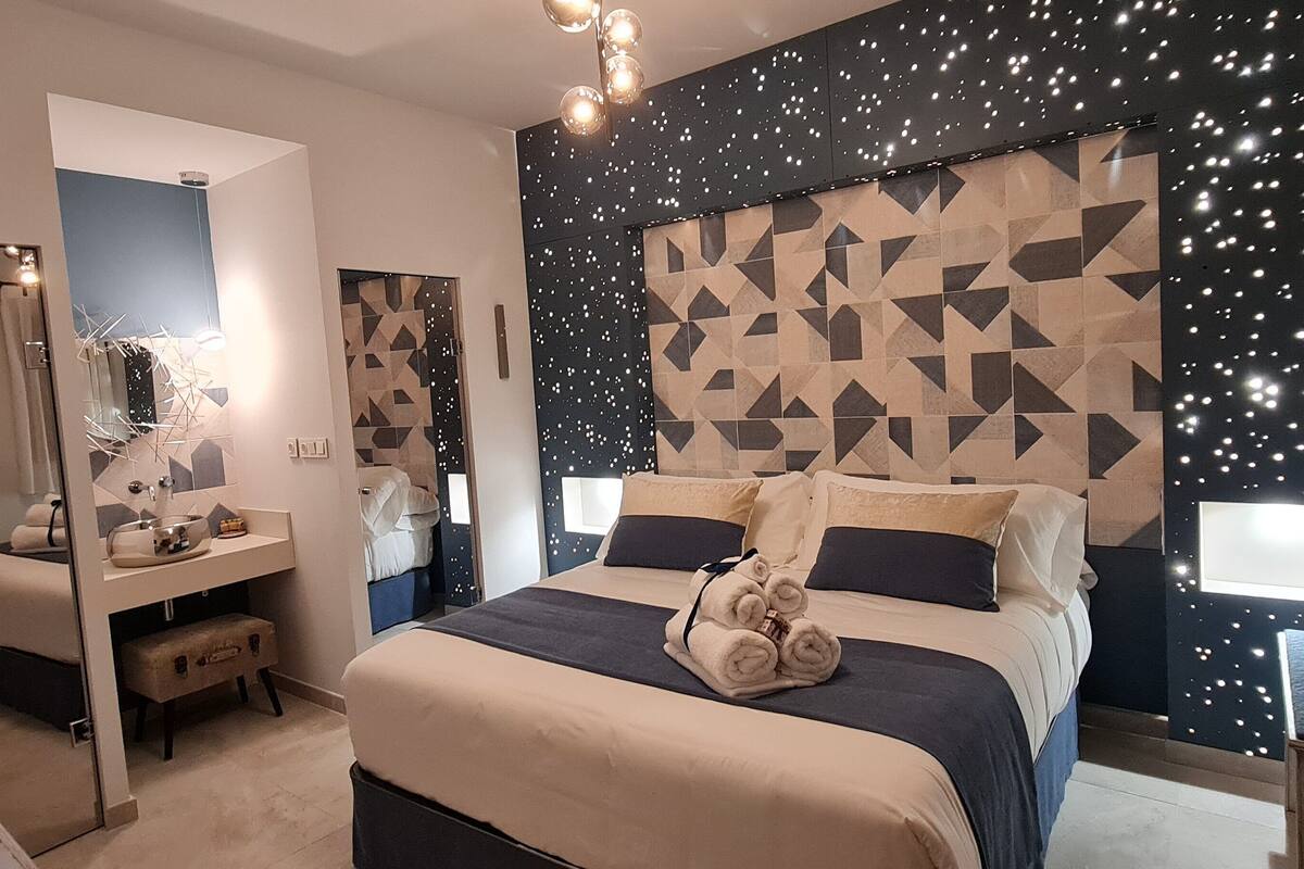 Una habitación de hotel moderna con una cama grande, un tocador con espejo y un cabecero de diseño geométrico.
