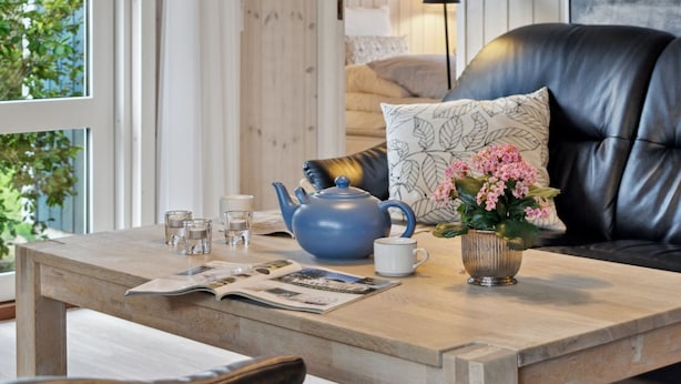 A cozy living room with a wooden coffee table, a blue teapot, a white mug, and a vase with pink flowers.