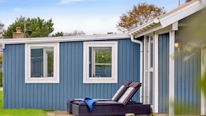 A small blue house with two windows and a patio area with a reclining chair and a table.
