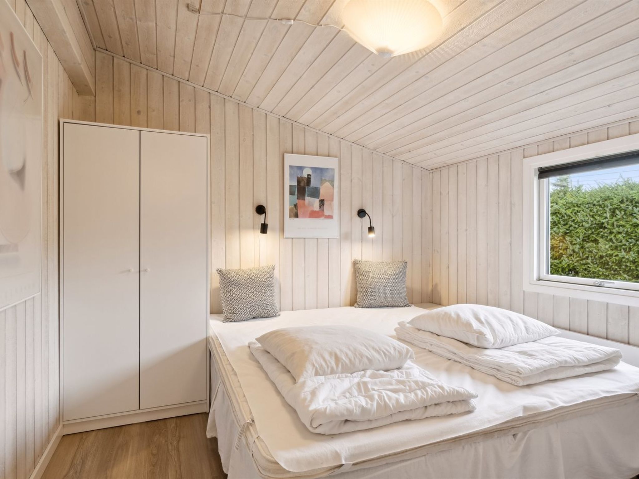 Um quarto com uma cama, duas mesas de cabeceira, uma janela e um guarda-roupa.