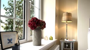A room with a window, a radiator, a lamp, and a vase with flowers on the windowsill. - 4 Bed House Sleeps 7 - Parking, Garden, Wifi (Killarney)