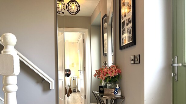 A hallway with a staircase, a mirror, a vase with flowers, and a small table with a sign and a bottle. - 4 Bed House Sleeps 7 - Parking, Garden, Wifi (Killarney)