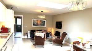 A modern living room with a sofa, chairs, a dining table, and a kitchen area with a red toaster. - 4 Bed House Sleeps 7 - Parking, Garden, Wifi (Killarney)