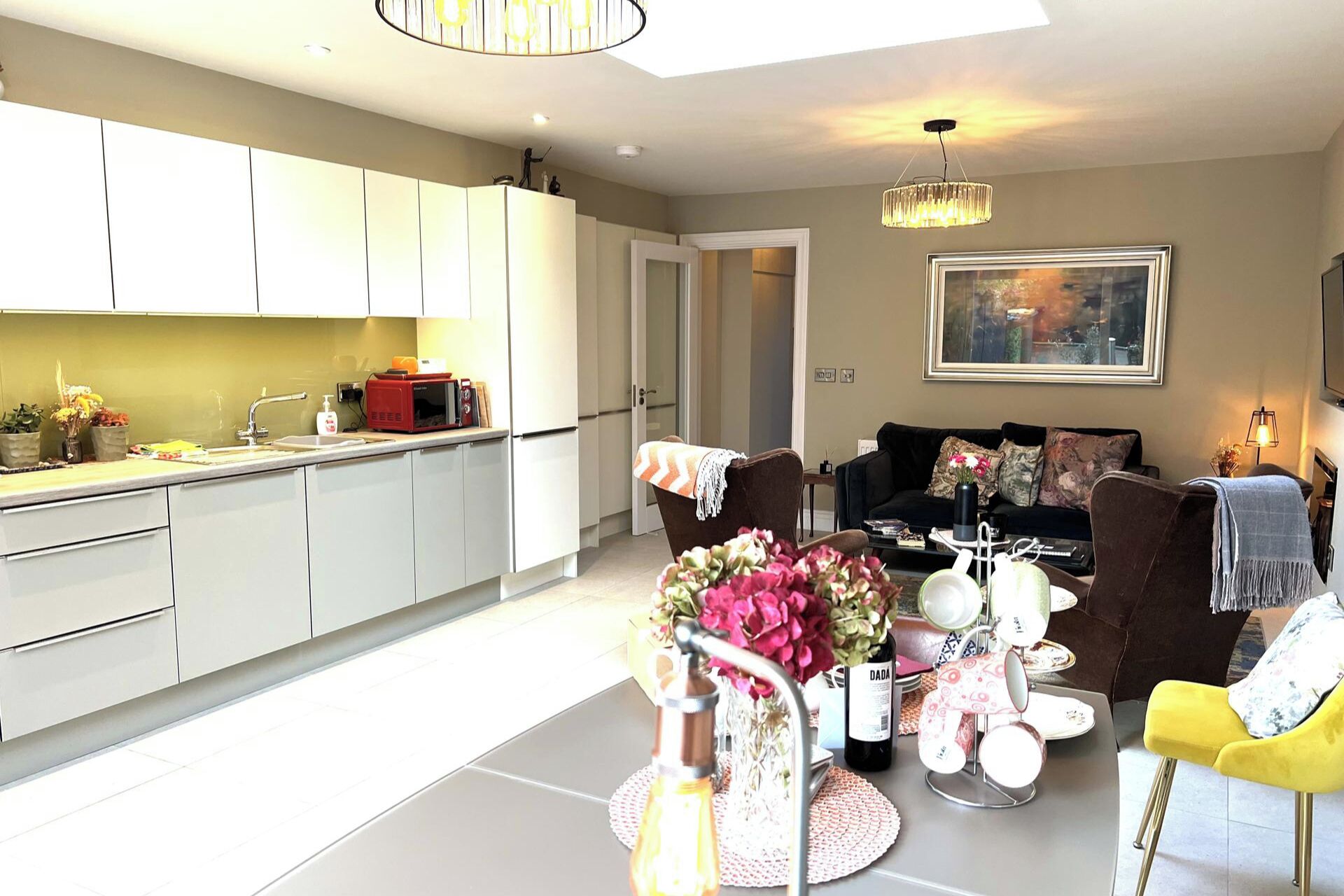 A modern kitchen with white cabinets, a dining area with a table set for four, and a living room with a sofa and a coffee table.
