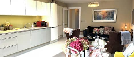 A modern kitchen with white cabinets, a dining area with a table set for four, and a living room with a sofa and a coffee table.