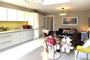 A modern kitchen with white cabinets, a dining area with a table set for four, and a living room with a sofa and a coffee table. - 4 Bed House Sleeps 7 - Parking, Garden, Wifi (Killarney)