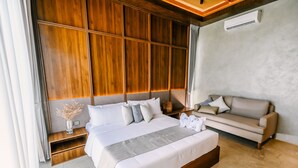 A modern hotel room with a large bed, a sofa, a wooden headboard, and a small side table with a vase. - TANA Beach Villas (Lian)