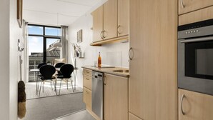 A modern kitchen with wooden cabinets, a dishwasher, and a built-in oven. - Nice apartment in Fanø with WiFi (Fanø)