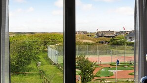 A view of a golf course with a fenced area, a building with a thatched roof, and a flagpole with flags. - Nice apartment in Fanø with WiFi (Fanø)