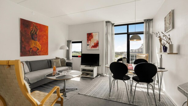 A modern living room with a sofa, coffee table, and dining area with chairs. There is a TV, artwork on the walls, and a large window with curtains. - Nice apartment in Fanø with WiFi (Fanø)