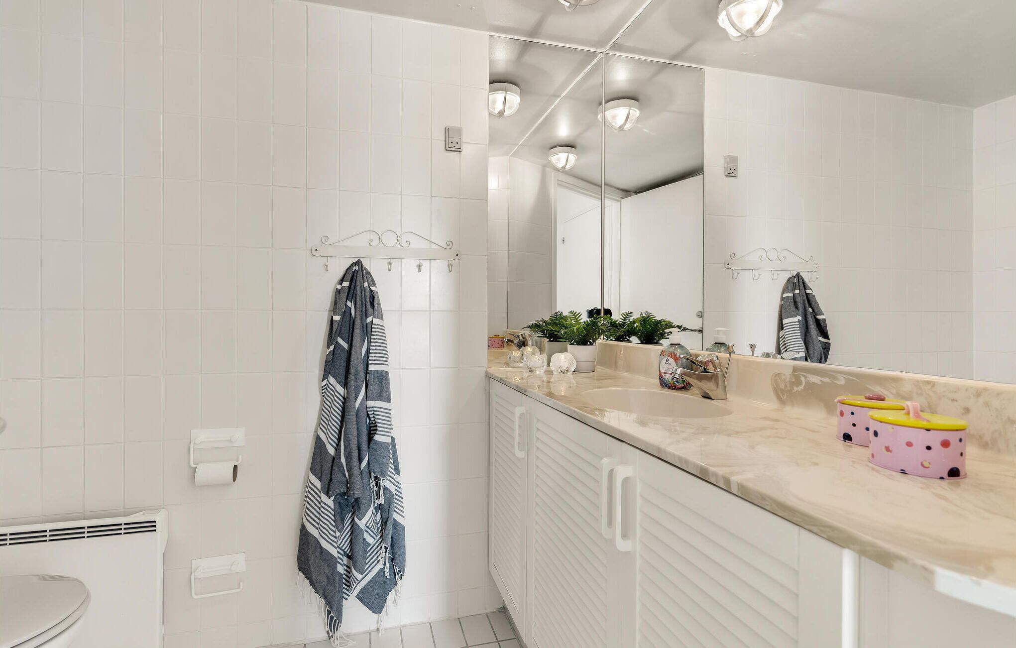 Een moderne badkamer met witte tegels, een grote spiegel, een wastafel met een beige aanrechtblad en een toilet.