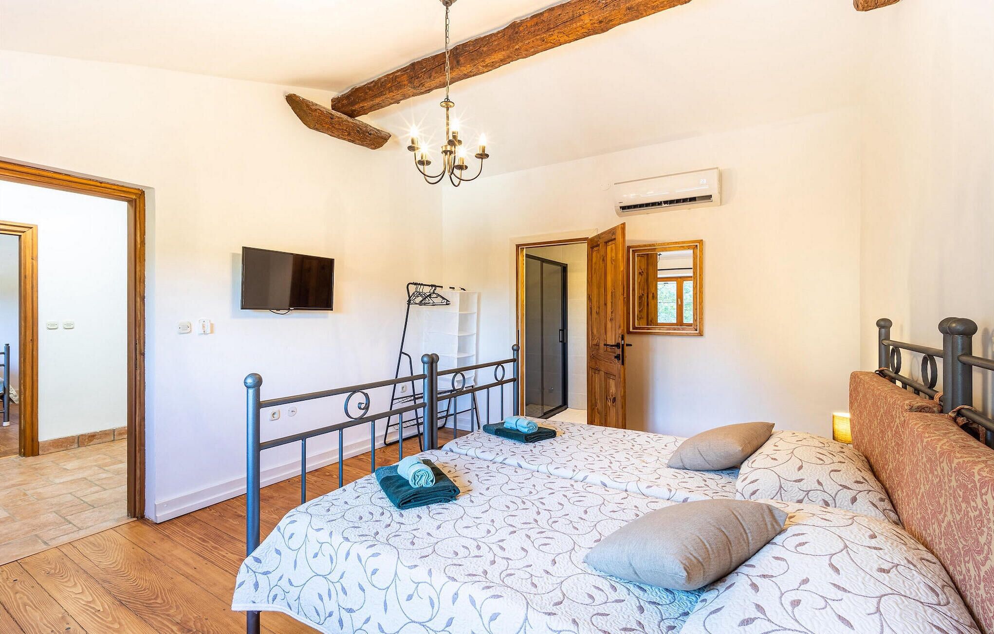 A bedroom with a bed, a TV, a wooden ceiling beam, and an air conditioning unit.