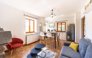 Cozy living space with a dining table, sofa, and kitchen area featuring a refrigerator, stove, and window with iron bars.