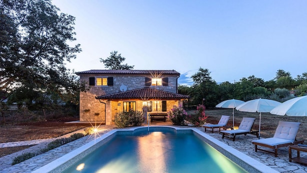 Una casa de piedra con piscina, zona de estar al aire libre y entrada bien iluminada.