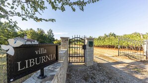Una villa llamada LIBURNIA, con un portón de piedra y un viñedo al fondo.