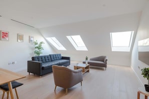 A modern loft apartment with a high ceiling, skylights, a grey sofa, a small table, and a potted plant.